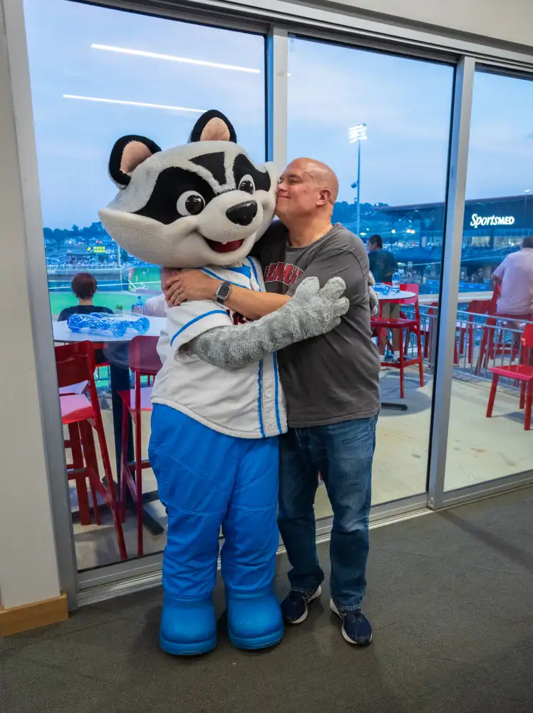 an employee of travel and tourism marketing agency Red Sage kisses the Rocket City Trash Pandas' mascot